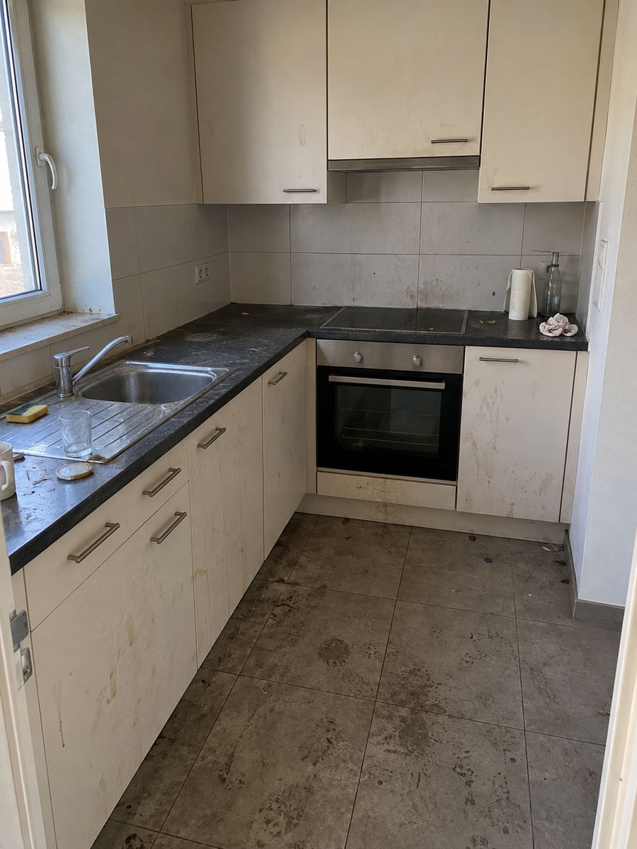 Cuisine d’un appartement de location à Blankenberge, vide de meubles mais sale, plans de travail gras, sol encrassé et objets abandonnés