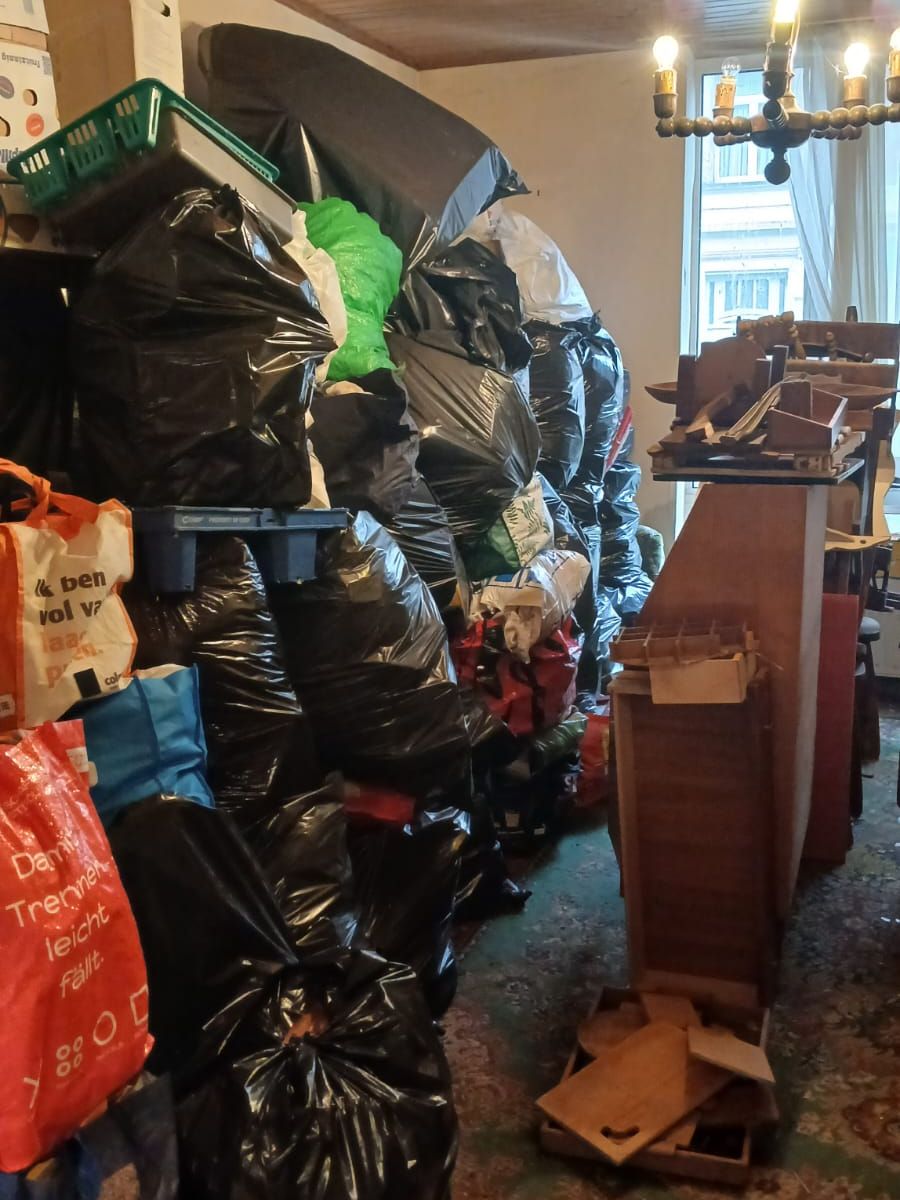 Salle à manger à Charleroi avec lustre en bois, sacs-poubelle empilés jusqu’au plafond et meuble en bois démonté