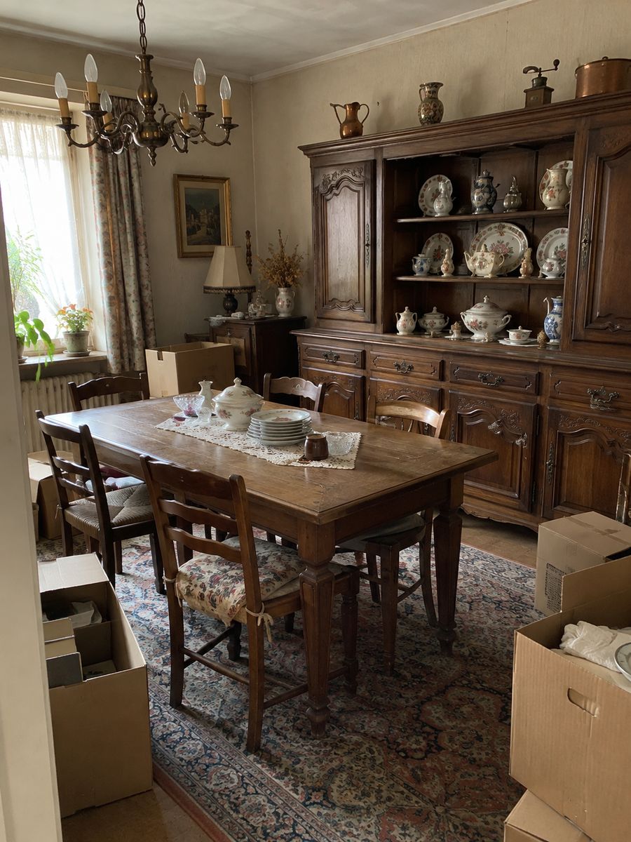 Salle à manger à l’ancienne d’un couple âgé avec buffet en bois, porcelaine, table, chaises et cartons