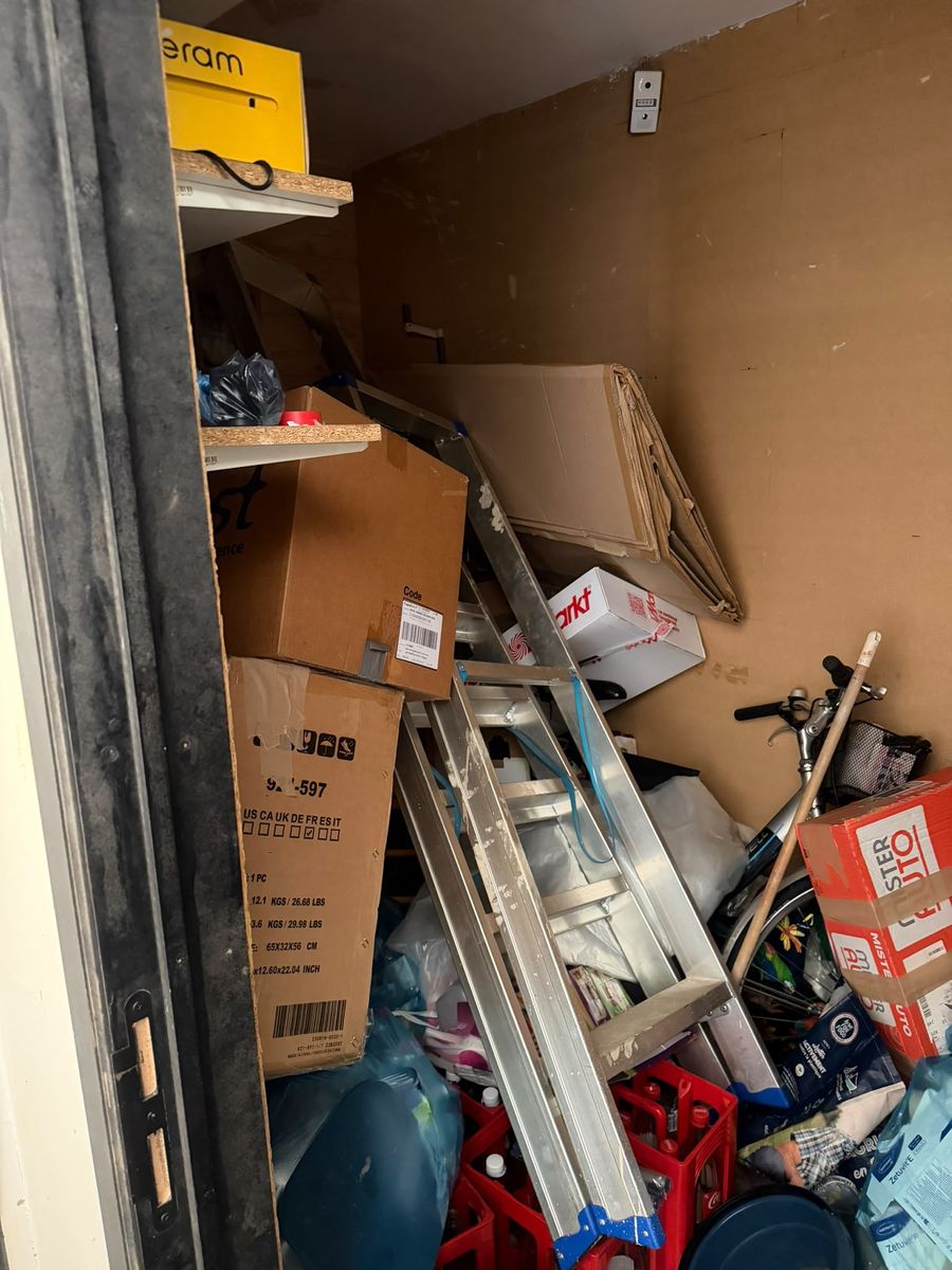 Réduit plein dans une maison de Namur : escabeau en aluminium, vélo, cartons, casiers de bouteilles et sacs